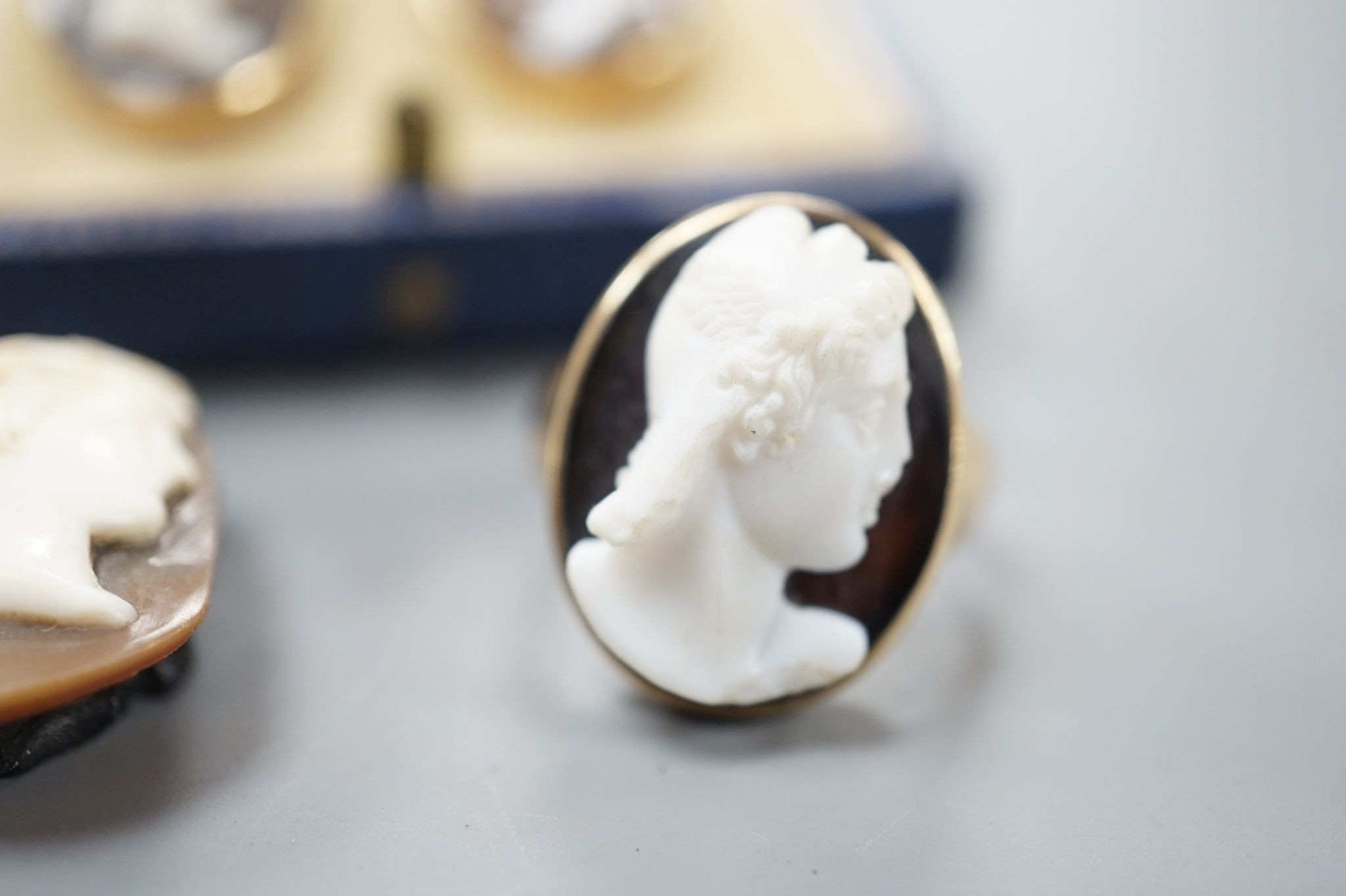 A yellow metal and hardstone set cameo ring, size J (a.f.), gross 6.9 grams, a pair of similar cameo shell ear clips and one other cameo shell mount.